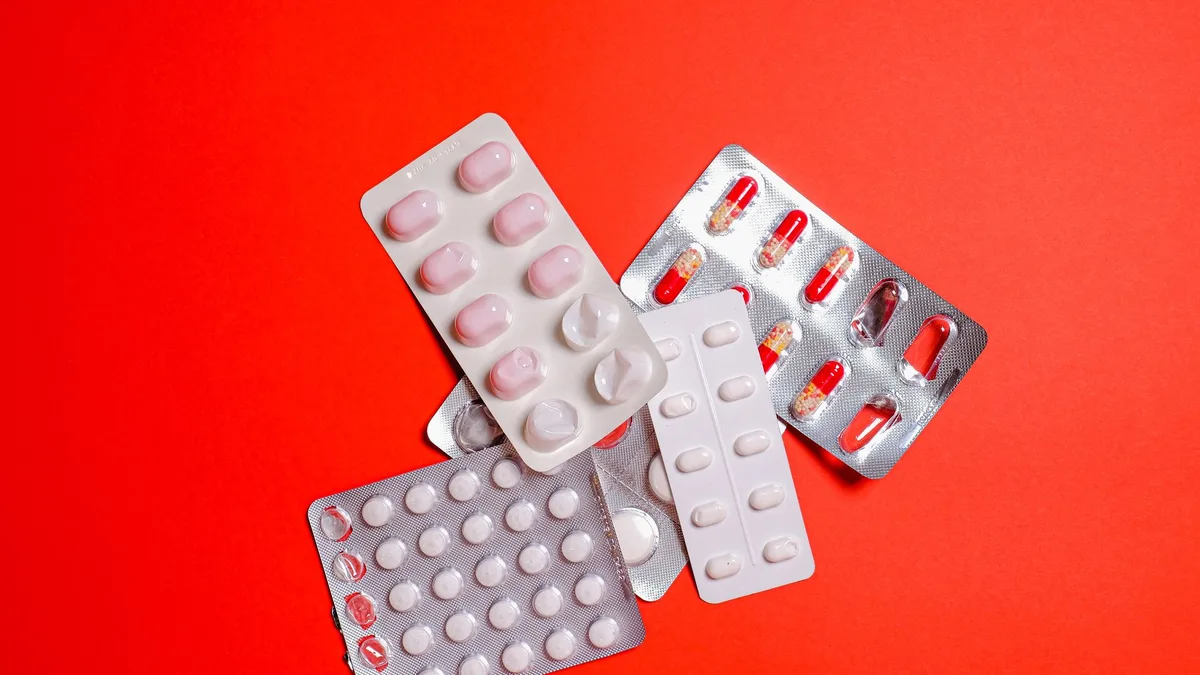 An assortment of pills and capsules in blister packs displayed on a vibrant red surface.