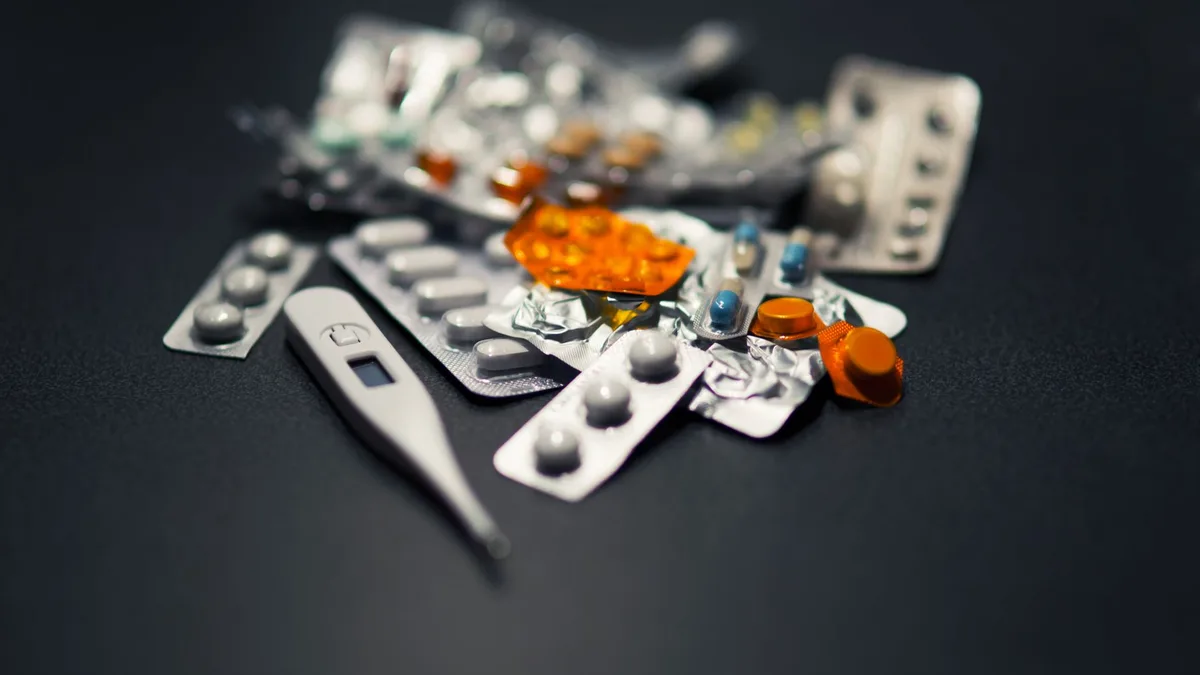 Close-up of various pills and a digital thermometer against a dark background.