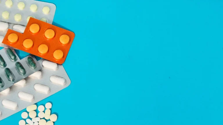 Colorful blister packs and loose pills on a blue backdrop with copy space.