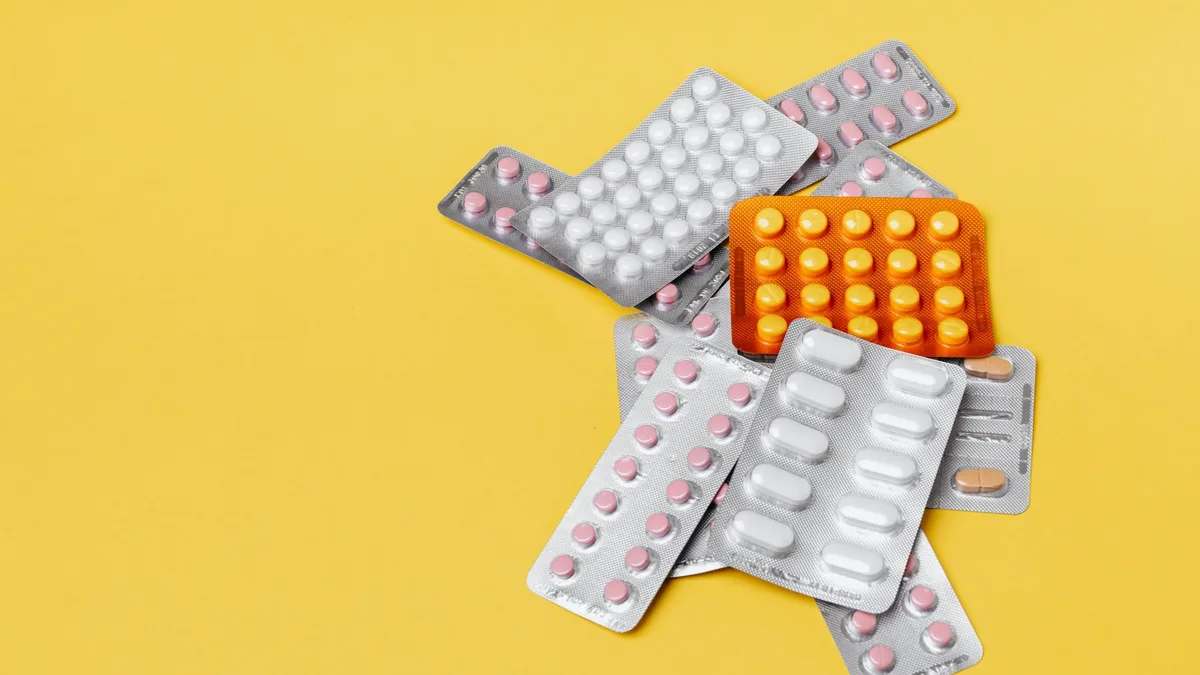From above of various medication blister packs of different color and shape on yellow background