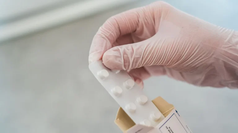 Close-up of a hand in gloves holding a blister pack of pills, symbolizing medical care.