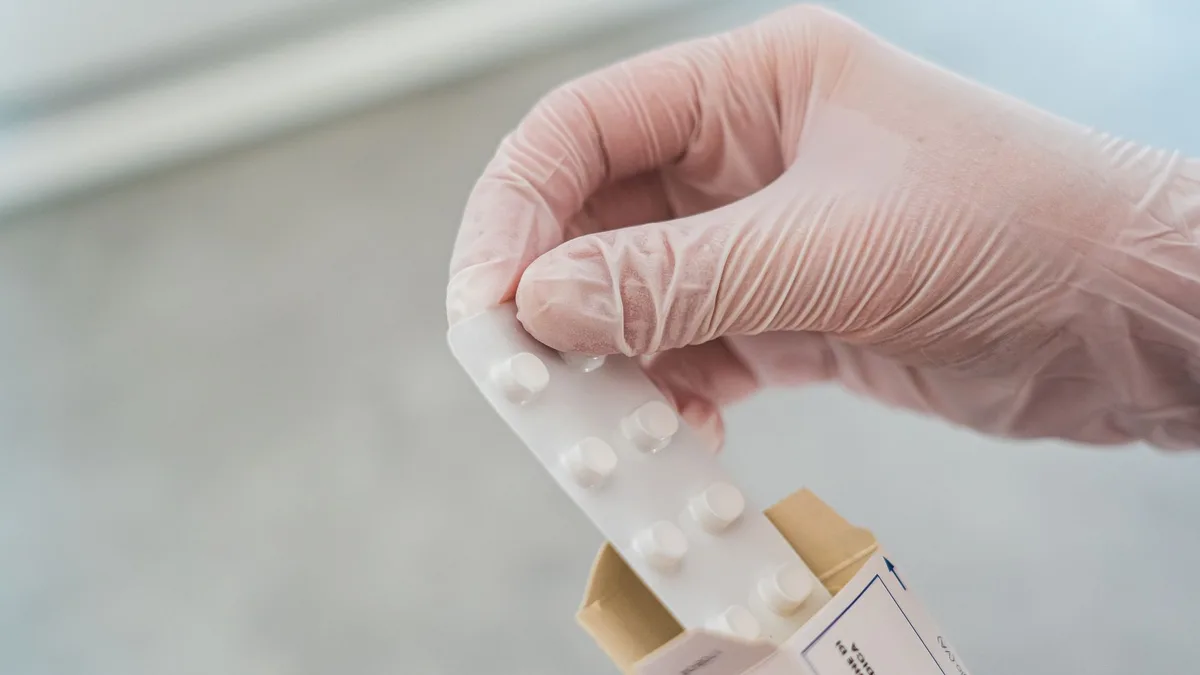 Close-up of a hand in gloves holding a blister pack of pills, symbolizing medical care.