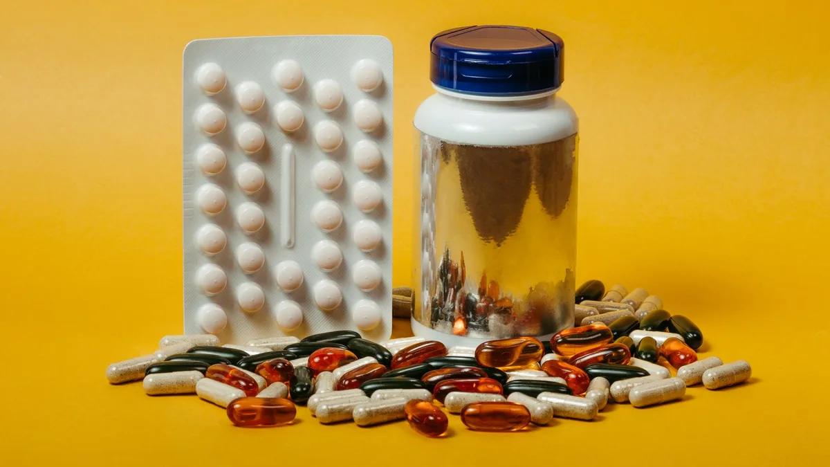 A variety of pills and capsules with a bottle on a vibrant yellow background, ideal for medical themes.