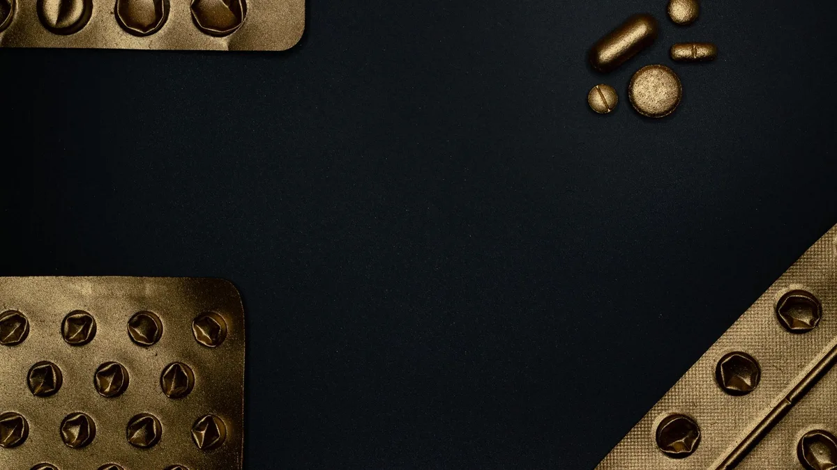 Golden blister packs and pills on a dark surface, offering contrast and copyspace.
