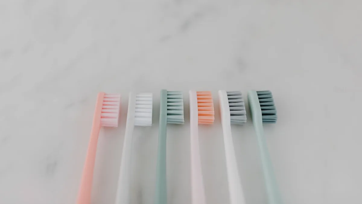A row of colorful pastel toothbrushes aligned on a smooth marble surface.