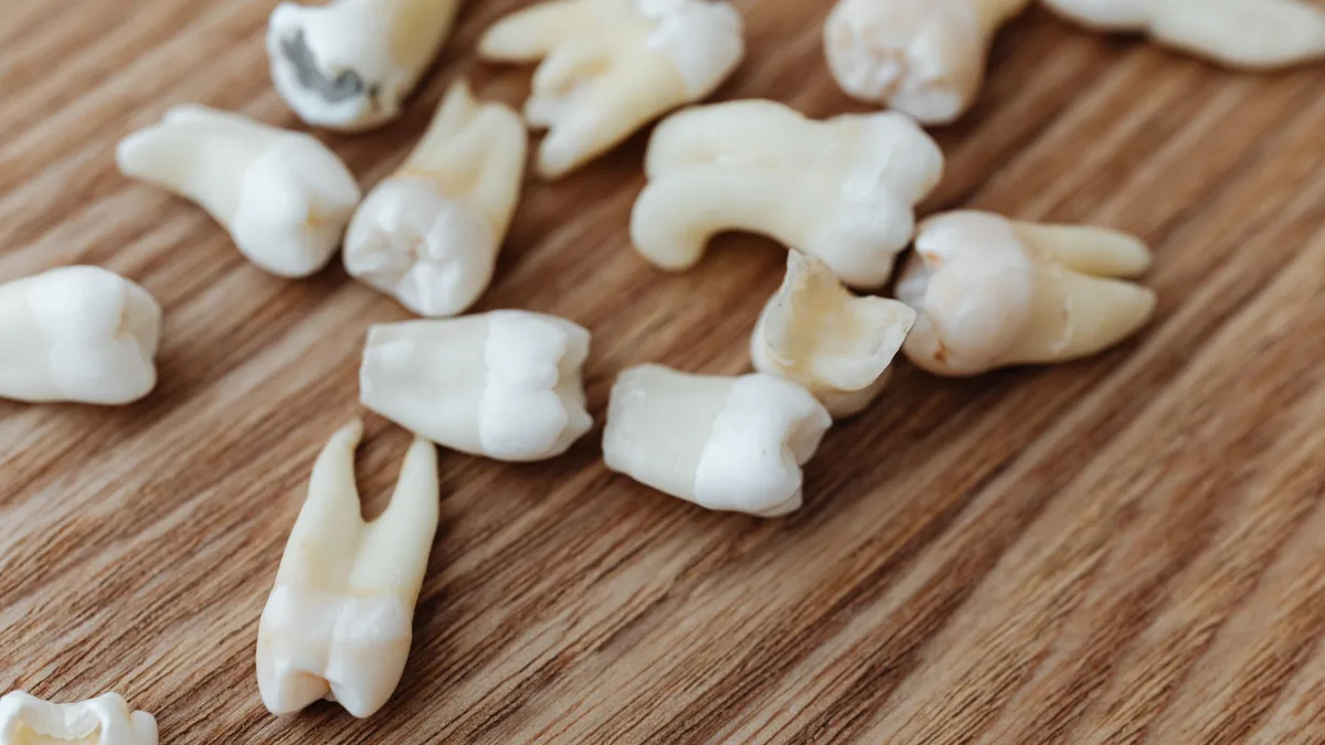 A detailed close-up of multiple extracted human teeth arranged on a wooden background surface.