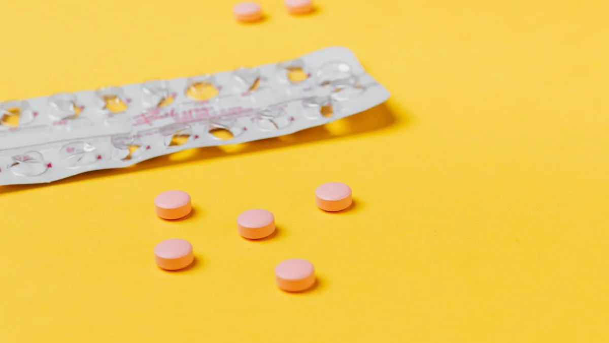 Pink pills scattered on a vibrant yellow background with an empty blister pack.