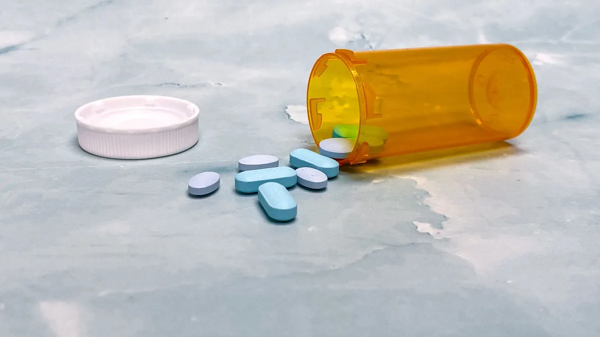 Scattered blue pills and an orange prescription bottle on a light surface.