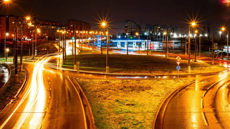 Long exposure of a city roundabout at night showcasing vibrant light trails and streetlights.