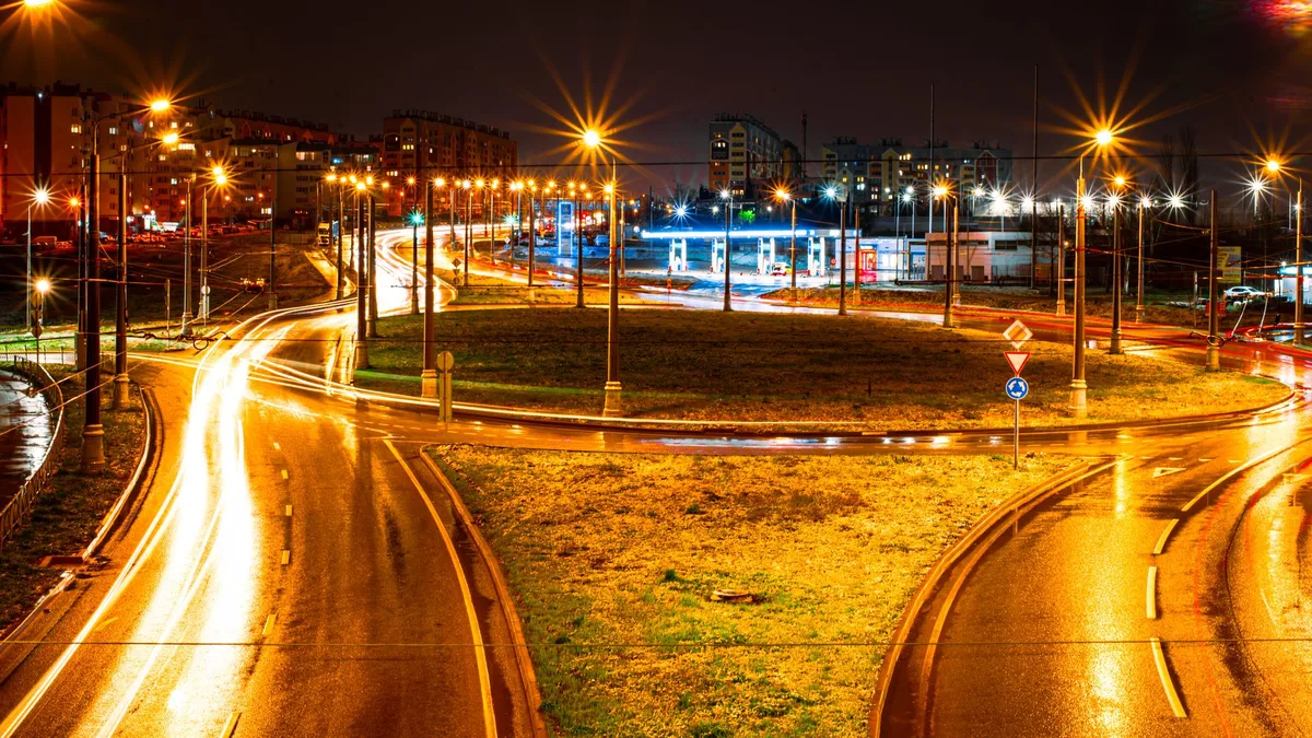 Long exposure of a city roundabout at night showcasing vibrant light trails and streetlights.