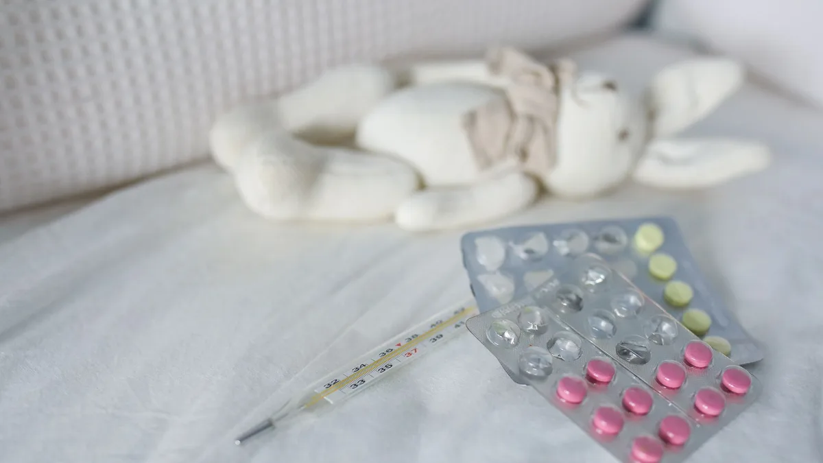 Close-up of medication and thermometer on a bed beside a plush rabbit toy, symbolizing childhood illness care.