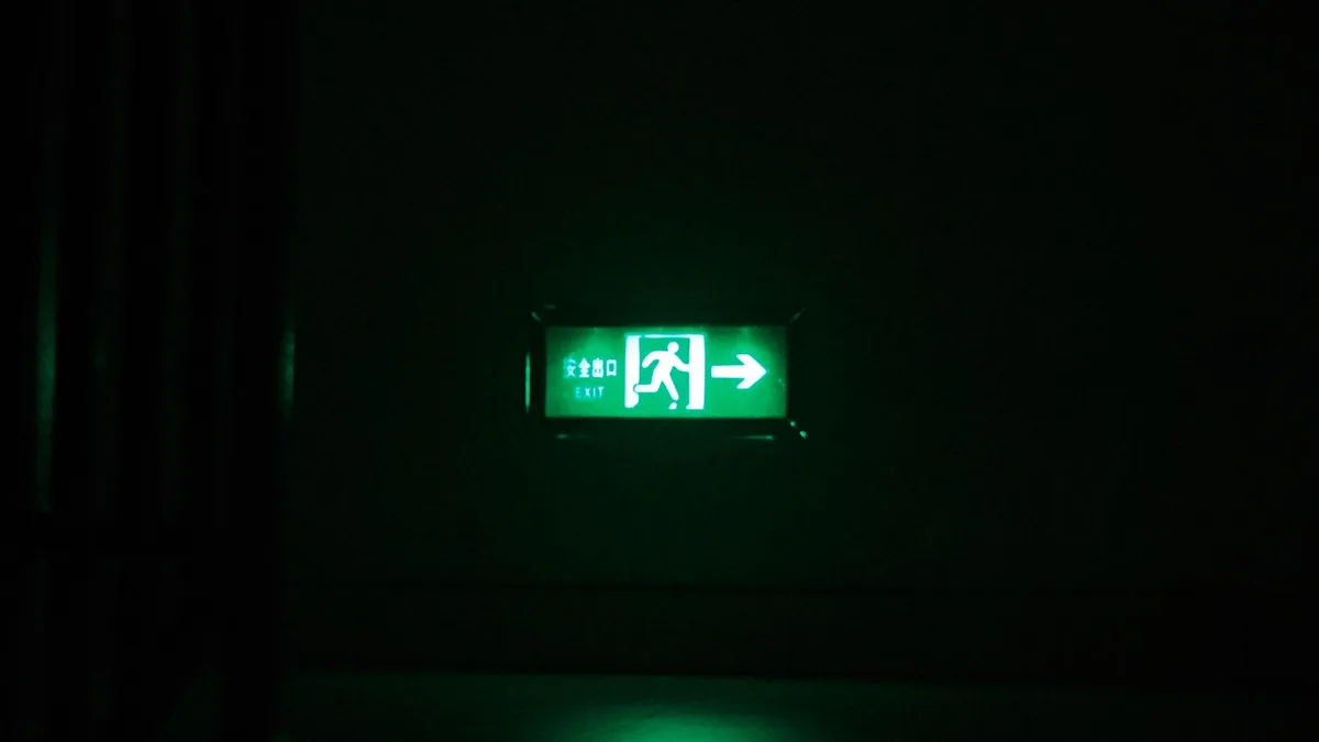 Illuminated green exit sign with directional arrow in a dark indoor setting.