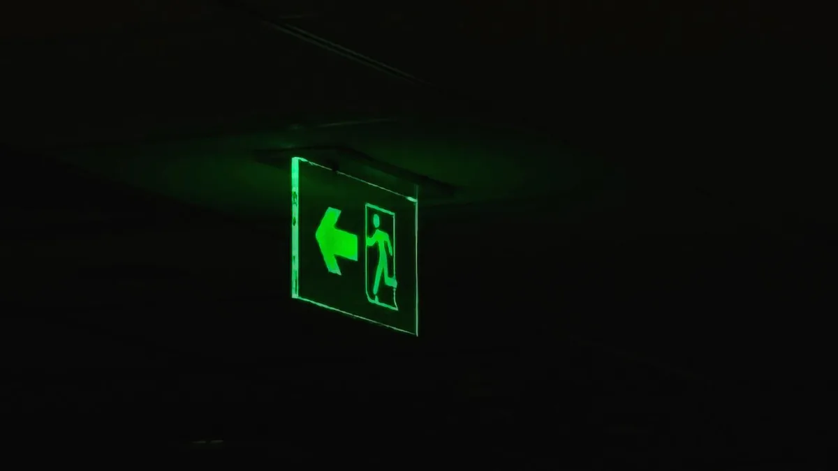 An illuminated green emergency exit sign with directional arrow in a dark setting.