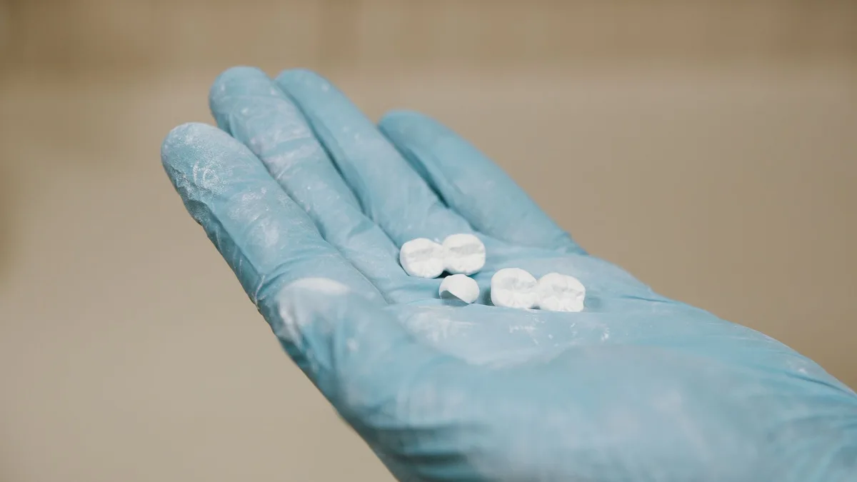 White artificial teeth for denture placed on hand in blue latex glove against light blurred background