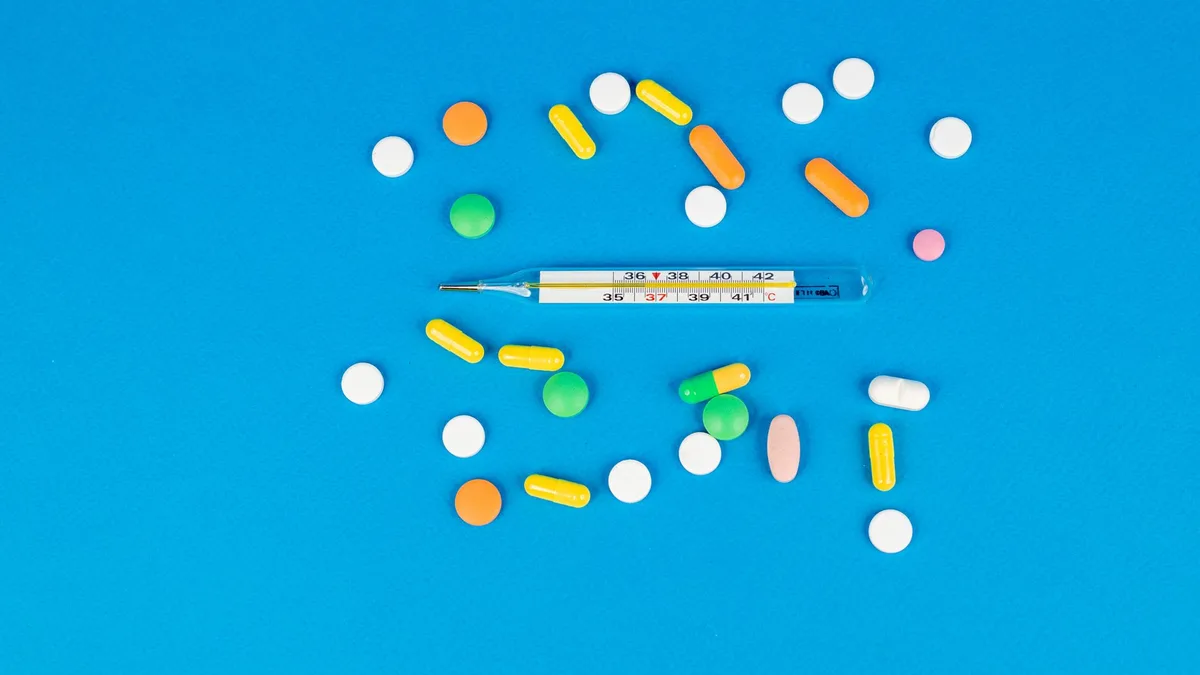 Vibrant pills and a thermometer arranged on a blue backdrop. Perfect for health and medicine themes.