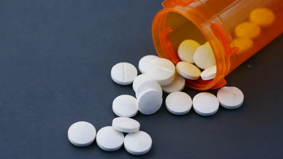 Close-up of white pills scattered from an orange prescription bottle on a gray surface.
