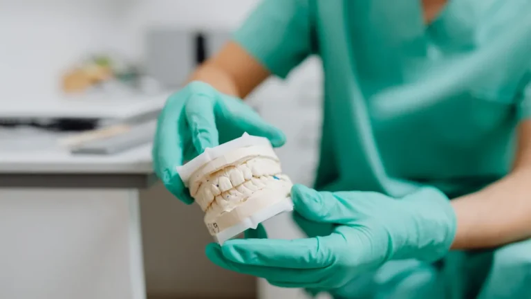 A close-up of hands in latex gloves holding a dental cast in a dental office.