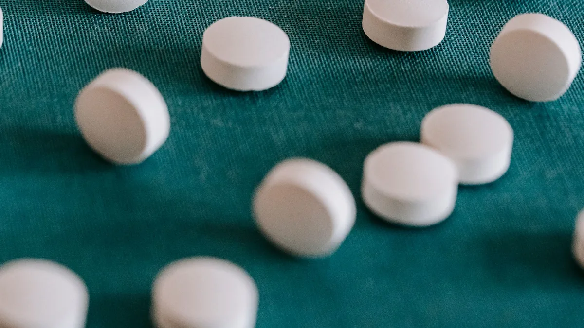 Closeup of similar round white pills spilled on green tissue in random order