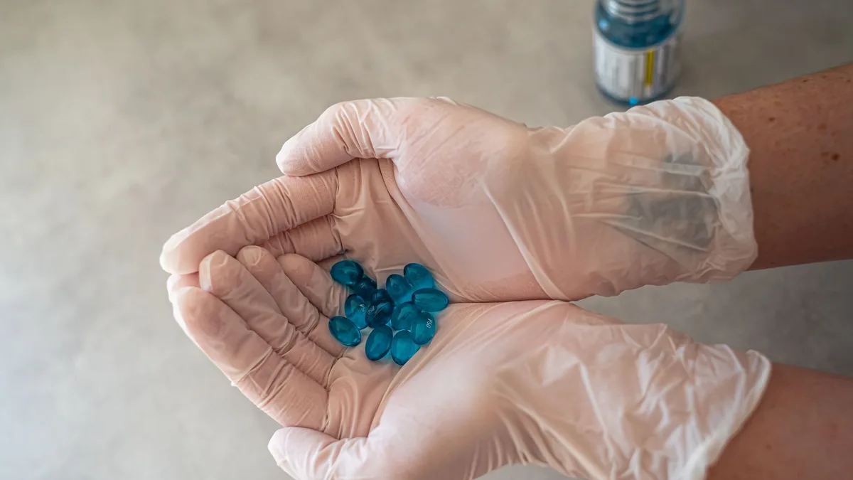 Close-up of gloved hands holding blue capsules, representing healthcare and medication.