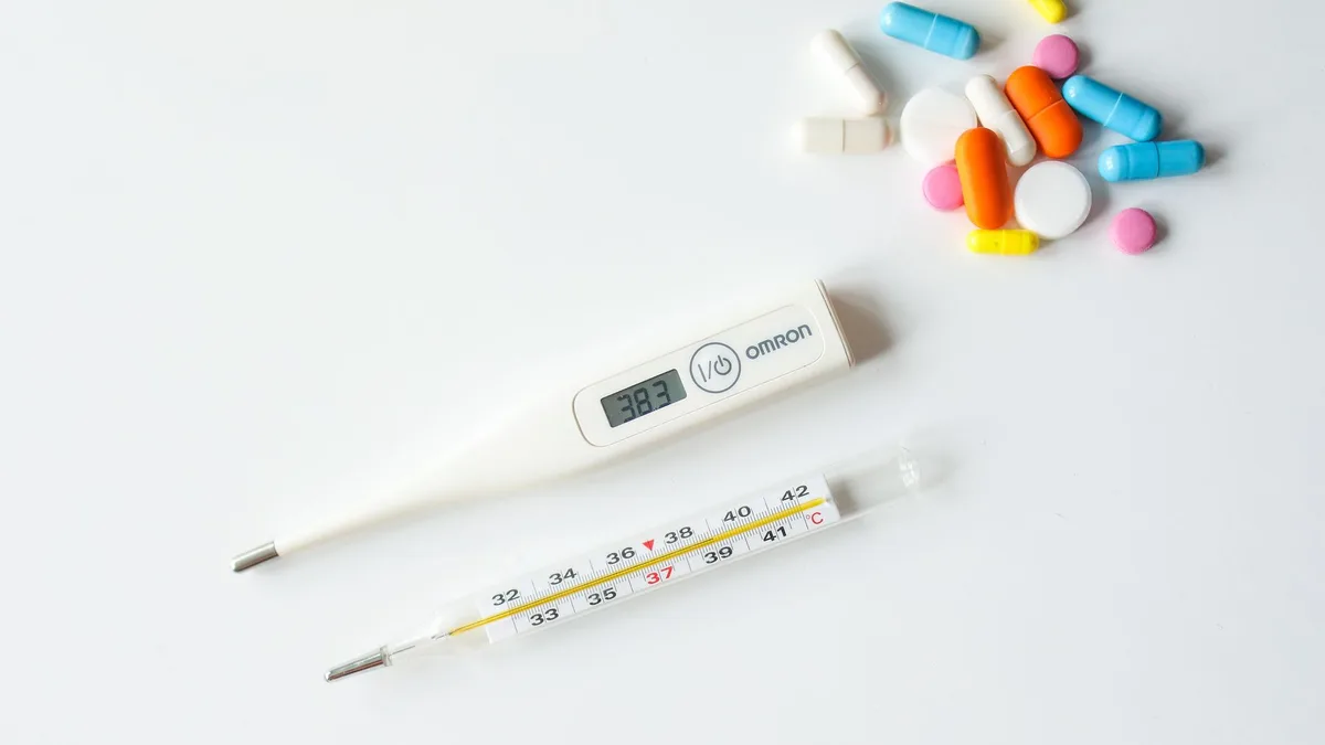 Digital and glass thermometers with colorful pills on white background.