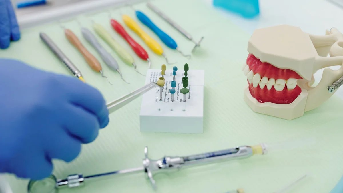 From above of crop faceless orthodontist in latex gloves and tweezers working at medical table with cast jaw and set of syringes near periodontal scalers