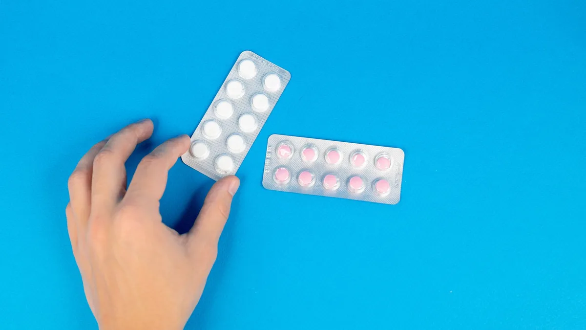 Image of a hand reaching for blister packs against a blue background, offering copy space.